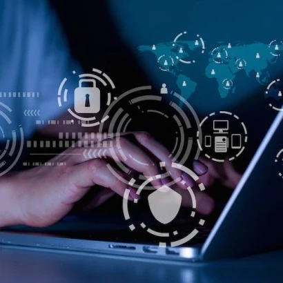 A close up of hands typing on a laptop with security icons floating around.