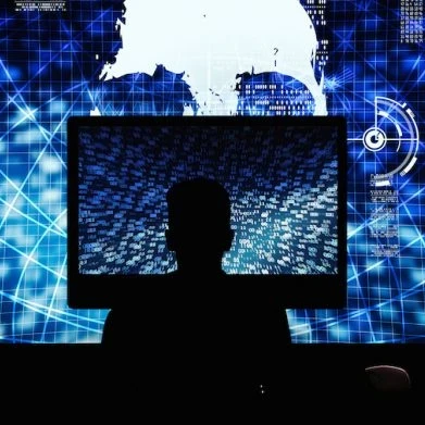 Hacker working on a large computer with additional screens next to them and a very large screen in front