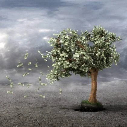 Image of a desert with a tree with dollar bills for leaves blowing away in the wind