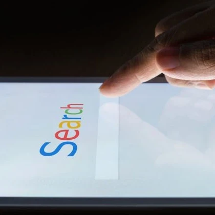 'Search' written in Google font and colours on a touchscreen with a user tapping the search bar