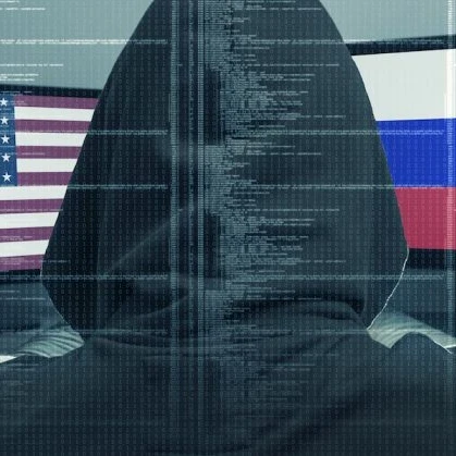 Back of a hacker in a black hoodie looking at two screens, one with the USA flag and the other with the Russia flag