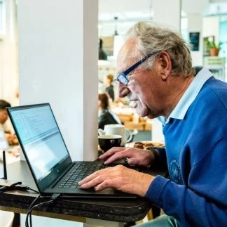 An elderly man sitting in front of a laptop.