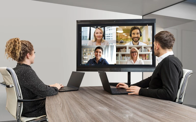 Hybrid meeting in progress. Two participants join the meeting from laptops in a meeting room, while four remote participants appear on a Avocor display